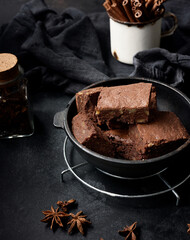 baked pieces of chocolate brownie cake with walnuts in a black metal frying pan on a wooden table, top view