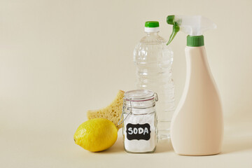soda jar, spray bottle, vinegar, lemon, wooden brush and sponge on beige background copy space