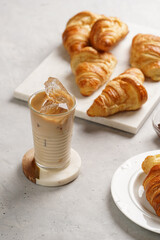 a glass with milk coffee and ice cubes, and freshly baked croissants on marble plate, brown hazelnut spread