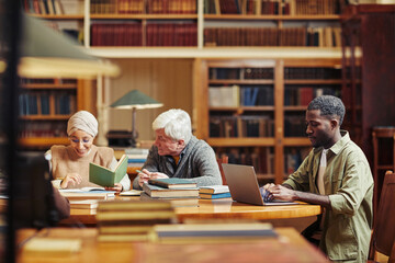 Side view portrait of young black man using laptop while studying college library with people in background