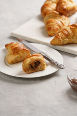A plate with butter croissant cut in half and several freshly baked french rolls on marble tray with hazelnut spread