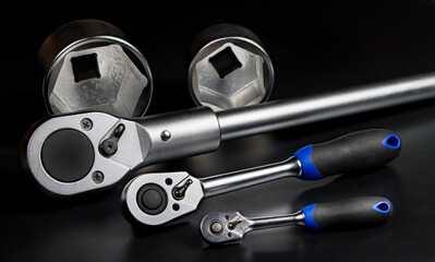 Closeup of metal ratchets and interchangeable hex sockets on black background. Three sizes of steel...
