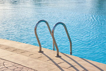 Close up of swimming pool stainless steel handrail descending into tortoise clear pool water....