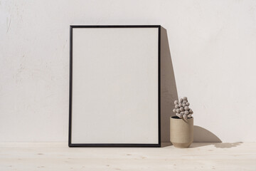 Poster frame and plant on bright beige wall. Stylish home decor design. Mockup