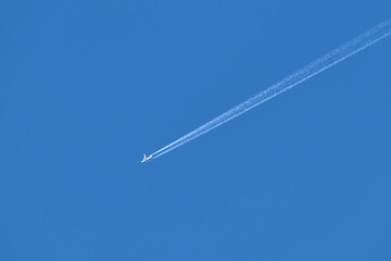 Distant passenger jet plane flying on high altitude on clear blue sky leaving white smoke trace of contrail behind. Air transportation concept