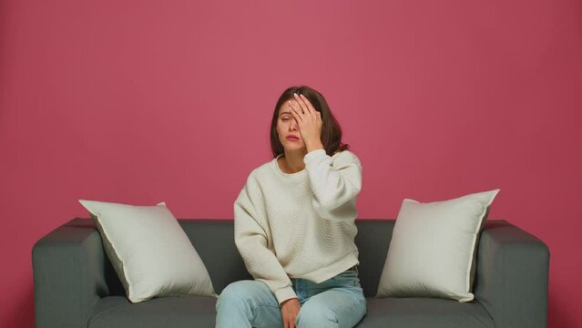 Funny emotional young girl resents, makes facepalm gesture, feeling shame, sitting on sofa, watching movie or series