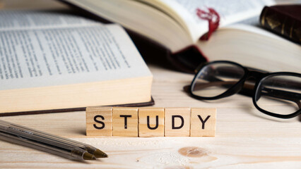 Word STUDY written with wooden blocks, along with pens, glasses and books on a table. Study and knowledge concept