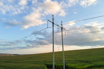 Fototapeta na wymiar High voltage tower with electric power lines between green agricultural fields. Transfer of electricity concept