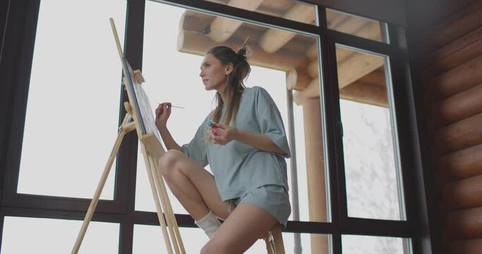 Art, creativity, hobby, job and creative occupation concept. Cute woman draws at home in bedroom near window in morning