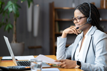 Young smiling african-american businesswoman in headset working remotely from home during maternity leave, selective focus. Pleasant black female remote recruiter communicating with candidates online