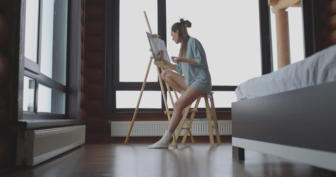 Art, creativity, hobby, job and creative occupation concept. Cute woman draws at home in bedroom near window in morning