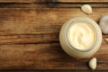 Jar of delicious mayonnaise and fresh garlic on wooden table, flat lay. Space for text