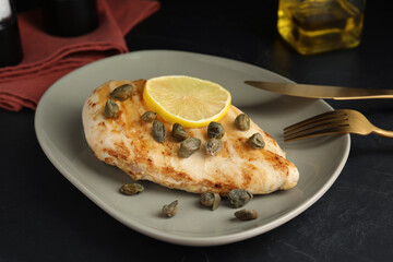 Delicious chicken fillet with capers and lemon served on black table, closeup