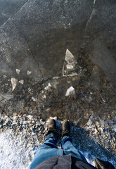 A man stands on frozen Lake with transparent ice with deep cracks. Beautiful winter landscape with clean, smooth. Top view of the legs with winter shoes