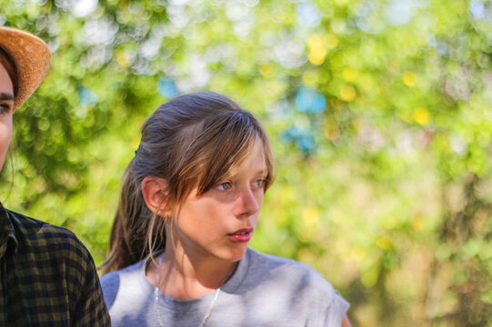 Defocused close-up preteen serious warried blond caucasian girl. Summer blurred green nature bokeh background. Portrait of handsome confused girl. Out of focus