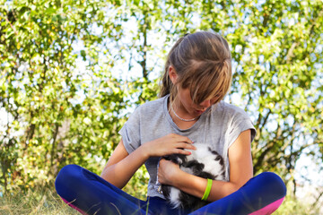 Fototapeta premium Defocus blonde little girl holding and caress cat, black and white small beautiful kitten. Nature green summer background. Girl holding and stroking pet, talk it. Love animals concept. Out of focus