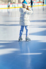 Rear view of girl in white tracksuit ice skating on skating rink outside. Healthy winter outdoor activities