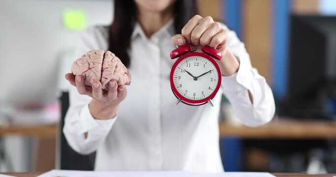Woman holds out alarm clock and model of human brain