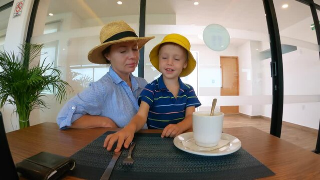 Timelapse of mother and her son having dinner in a cafe talking and smiling. The 4 years old boy is trying to use knife and fork and feed his mother. Nice time together