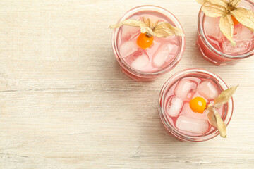 Refreshing cocktail decorated with physalis fruits on wooden table, flat lay. Space for text