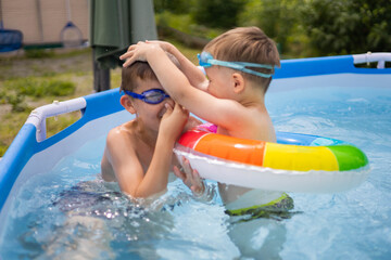 Two boys brothers in the outdoor outdoor pool near the house swim and play. Colored, swimming, bright, rainbow circles.