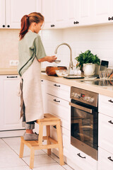 Cute teenage girl in kitchen apron prepares and kneads products for making dough for baking