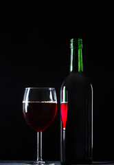 A glass of wine is reflected in the bottle on a dark background. The concept of drinking wine.