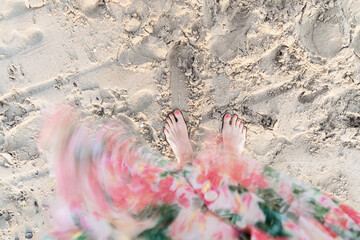 Frau blickt auf Füße am Strand, Kleid weht im Wind