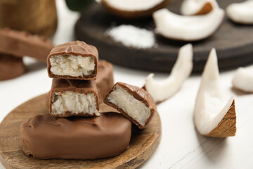 Delicious milk chocolate candy bars with coconut filling on white wooden table, closeup