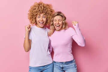 Overjoyed two young women clench fists celebrate something exclaim from joy wear casual clothes...