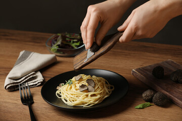 Woman slicing truffle onto spaghetti at wooden table, closeup