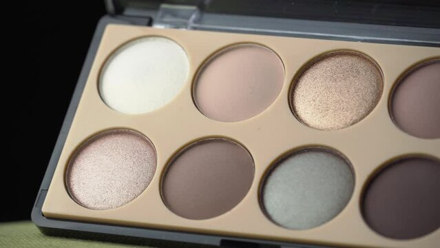 Glitter eye shadow swirls against a black background. New untouched cosmetics in a nude color. Makeup palette set. Professional multi-color eyeshadow palette. Close-up 4K