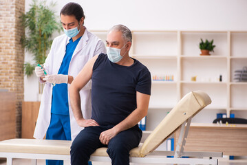 Obraz premium Old man visiting young doctor in covid-19 vaccination concept