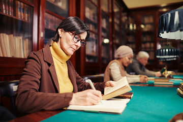 Portrait of adult woman studying in classic library interior by lamp light, copy space