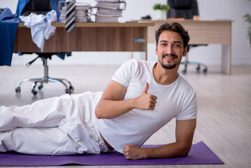 Fototapeta premium Young male employee doing sport exercises in the office