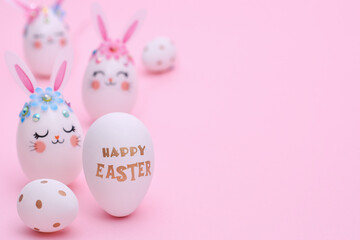 Pink Easter composition with copy space. Three white Rabbit Eggs with flowers, ears and muzzles on a pink background. Golden Greeting text Happy Easter on a white egg.