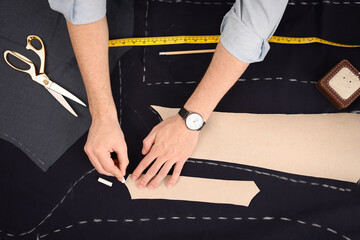 Tailor marking sewing pattern on fabric with chalk at table, top view