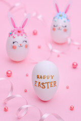 Happy Easter composition on a pink background. White eggs decorated with pink rabbit ears, flowers and muzzles of rabbits. Easter greeting card. Golden greetings text on a white egg: Happy Easter
