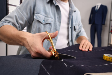 Tailor cutting fabric by following chalked sewing pattern at table in workshop, closeup