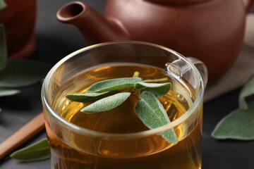 Cup of aromatic sage tea with fresh leaves on table, closeup
