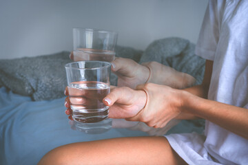 Woman holding glass of water in shaky hands and suffering from Parkinson's disease symptoms or...