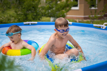 Two boys brothers in the outdoor outdoor pool near the house swim and play. Colored, swimming,...