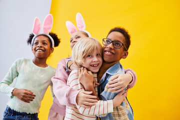 Diverse group of happy children celebrating Easter against bright yellow background in studio
