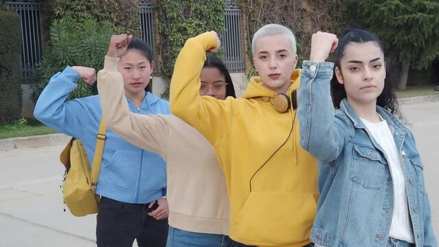 Group of young empowered women multiethnic looking at camera showing biceps. Feminism, empowered women