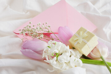 a bouquet of spring flowers in delicate shades, a small yellow gift box and a pink envelope on the bed