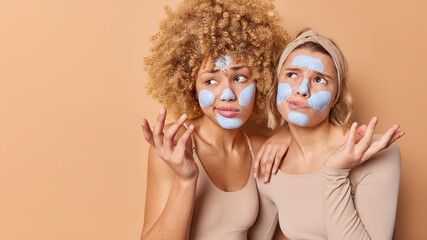 Hesitant confused young women shrug shoulders feel unaware apply beauty mask face difficult question stand against beige background blank space away for your advertising content Wellness concept