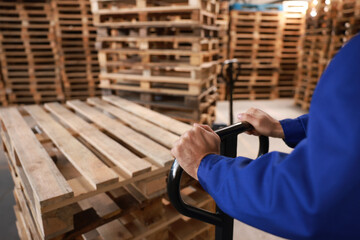 Worker moving wooden pallets with manual forklift in warehouse, closeup - obrazy, fototapety, plakaty