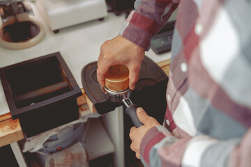 Fototapeta na wymiar Barista pressing ground coffee into portafilter with tamper