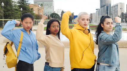 Group of young empowered women multiethnic looking at camera showing biceps.