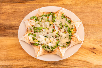 Pizza with lots of arugula, sliced Parmesan cheese and avocado with tomato slices